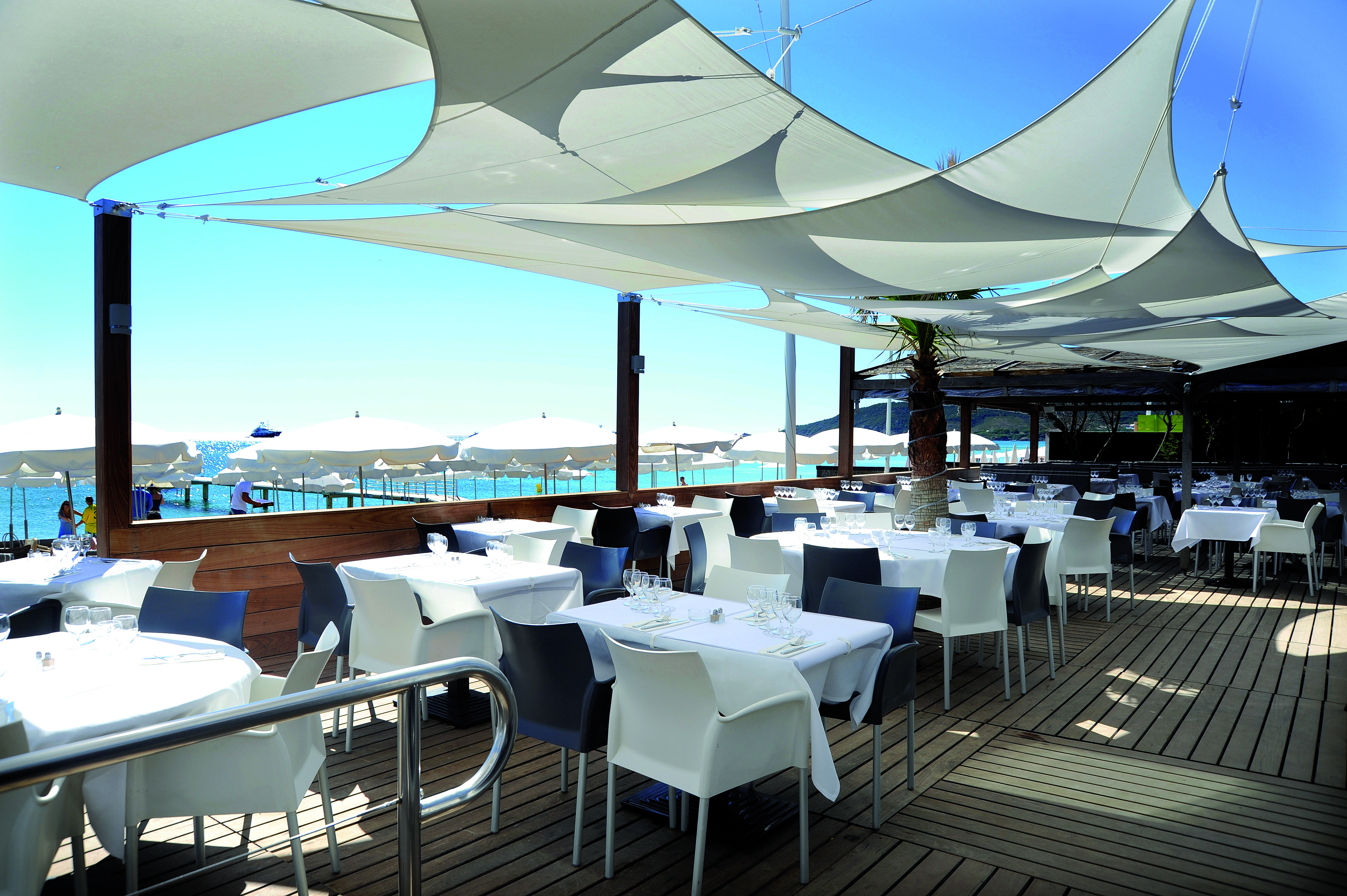 Voiles d'ombrages carrés et rectangulaire combinés pour ombragés une terrasse d'un restaurant au bord de mer